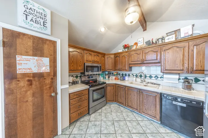 Kitchen featuring wood-finish cabinetry, stainless steel appliances, tiled countertops, and a patterned tile backsplash