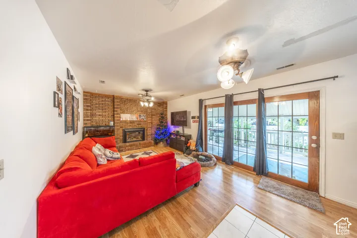 Living area featuring a brick accent wall with a built-in fireplace, wood-finish flooring, and a ceiling fan