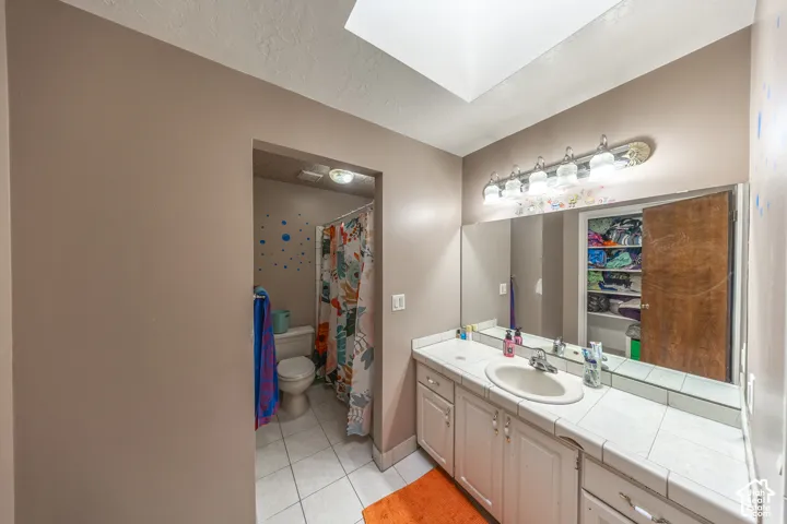 Bathroom featuring a single vanity with a white tile countertop, an undermount sink, a large wall-mounted mirror, and a five-light vanity fixture