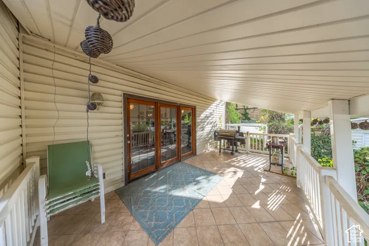 Covered porch featuring a tiled floor, white railing, and wood-framed glass patio doors