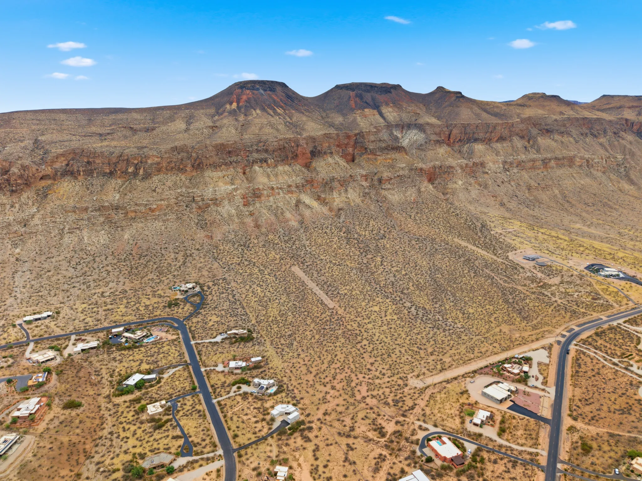 Expansive desert landscape featuring rugged mountain formations, scattered residential properties, paved roads, and natural vegetation