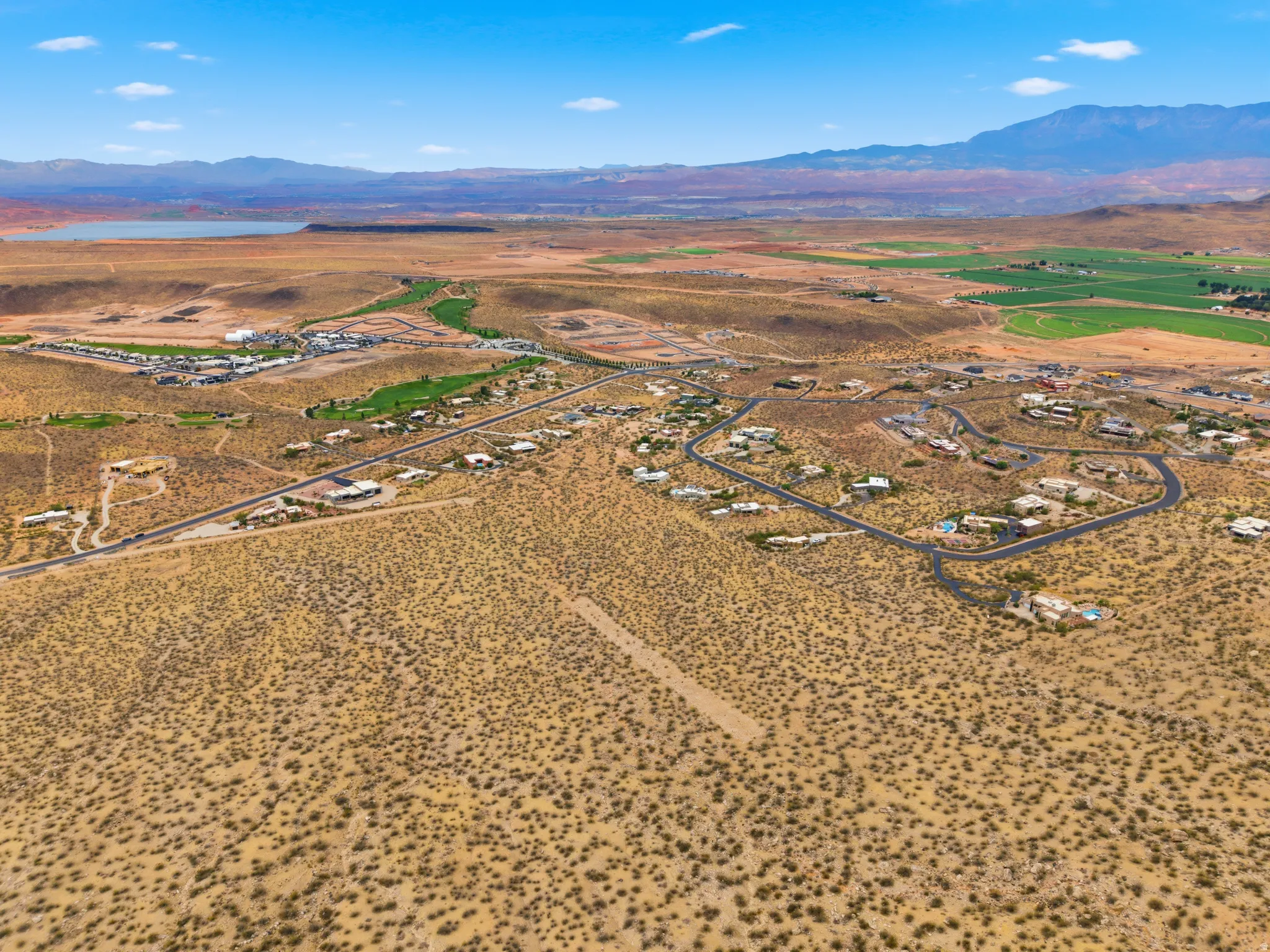 Expansive desert landscape featuring residential development, a distant body of water, and green fairways