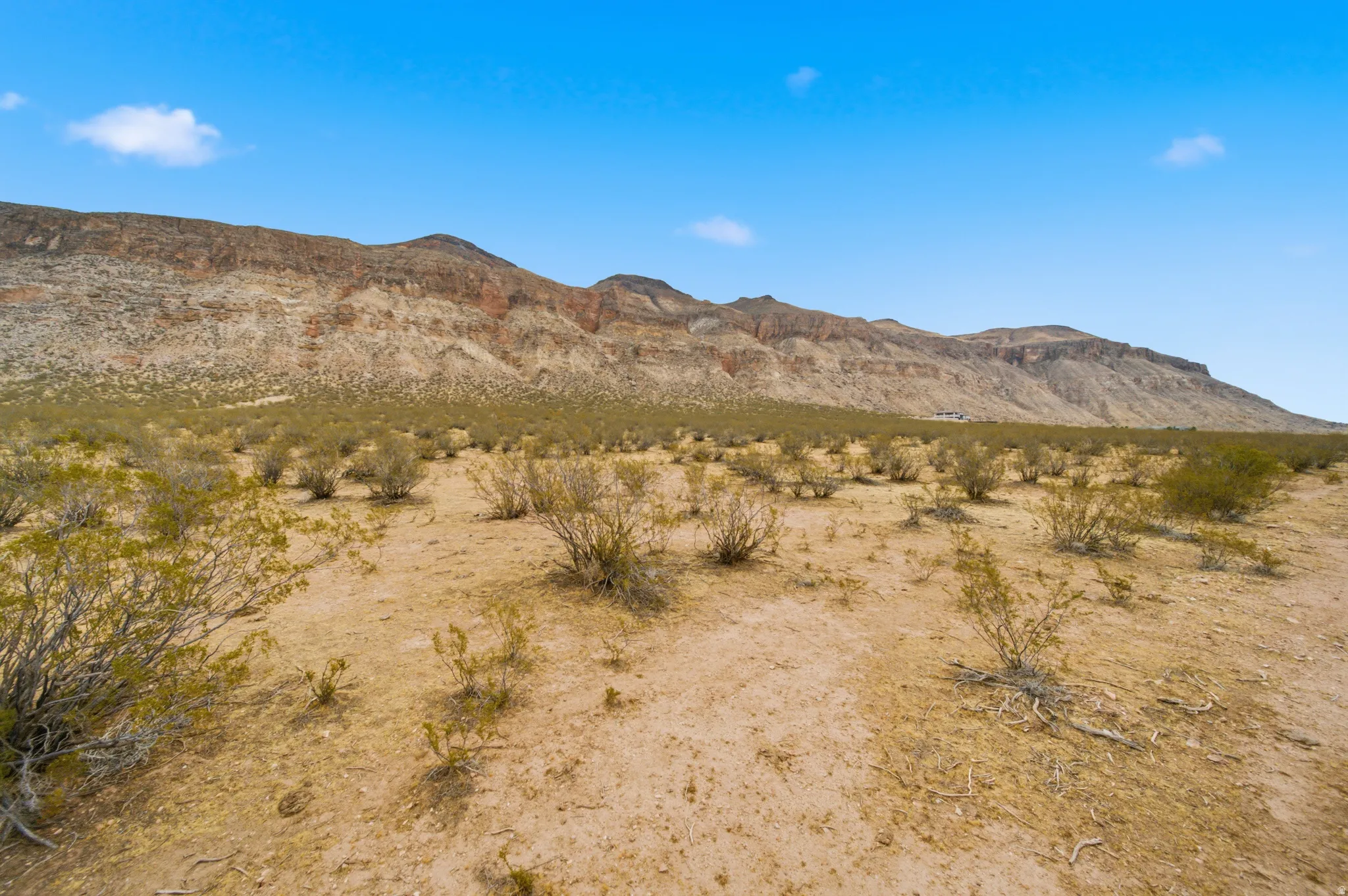 Expansive desert landscape featuring rugged mountain formations, natural scrub brush, and a vast open terrain