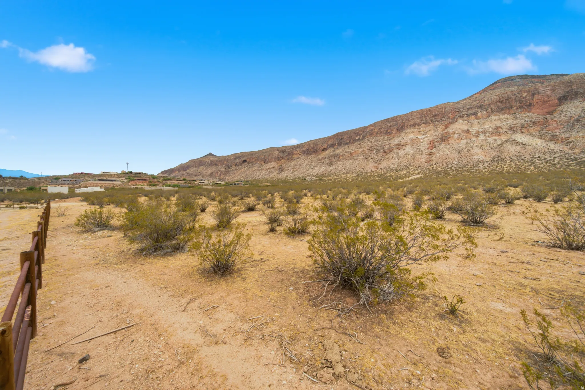 Expansive desert landscape featuring natural brush, a wooden fence line, and distant mountain terrain under a clear sky