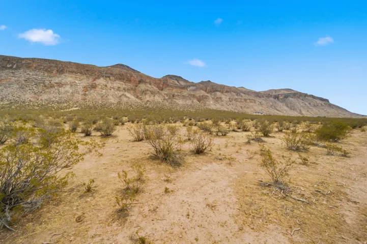 Expansive desert landscape featuring rugged mountain formations, natural scrub brush, and a vast open terrain