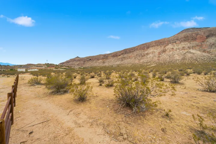 Expansive desert landscape featuring natural brush, a wooden fence line, and distant mountain terrain under a clear sky