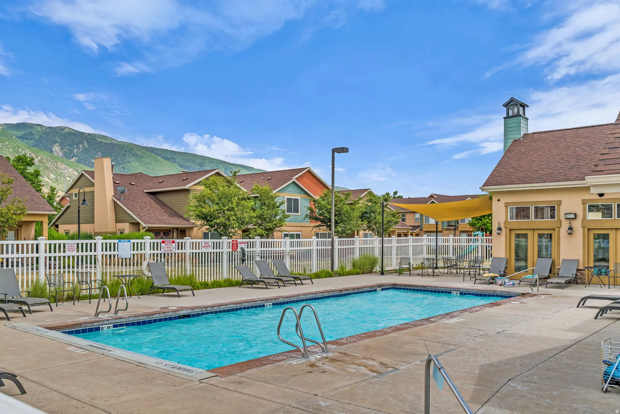 Rectangular outdoor pool with concrete surround, white perimeter fencing, and a nearby building featuring a cupola