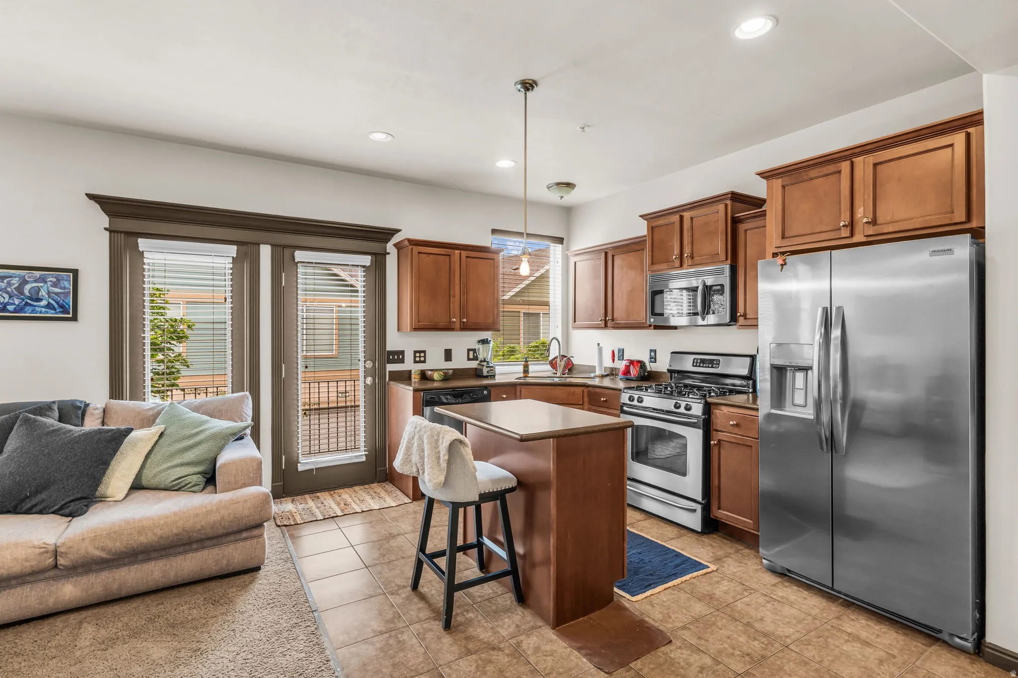 Kitchen featuring stainless steel appliances, wood-finish cabinetry, tile flooring, and a kitchen island with seating