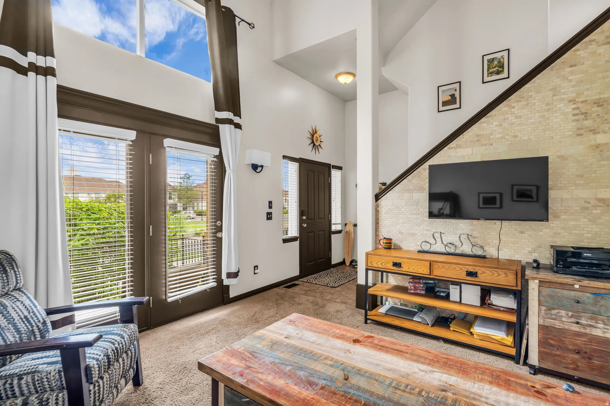 Vaulted ceiling living area featuring double French doors, transom windows, a textured accent wall, and wood-finish flooring