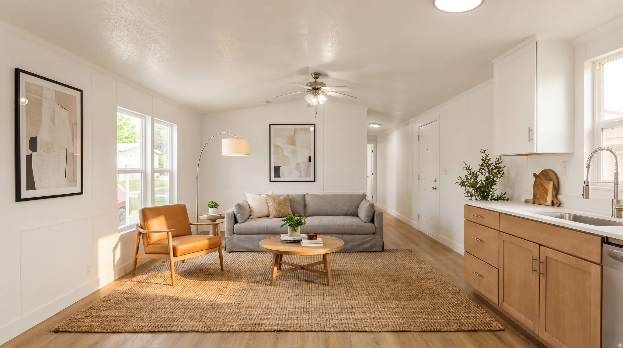 Open-concept living area featuring wood-finish flooring, white paneled walls, a ceiling fan, a kitchen with light wood cabinetry, and a white countertop with a subway tile backsplash