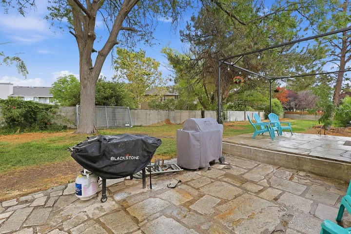 Expansive backyard featuring a natural stone patio and mature trees.
