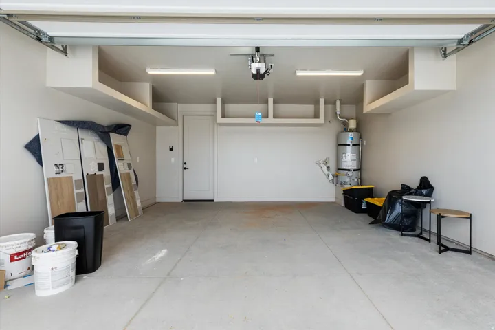 Concrete floor garage featuring a white overhead door, overhead lighting, an interior access door, and a water heater