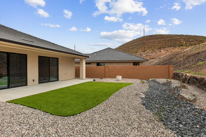 Rear exterior featuring stucco finish, tiled roofing, a concrete patio, artificial turf, and decorative gravel landscaping
