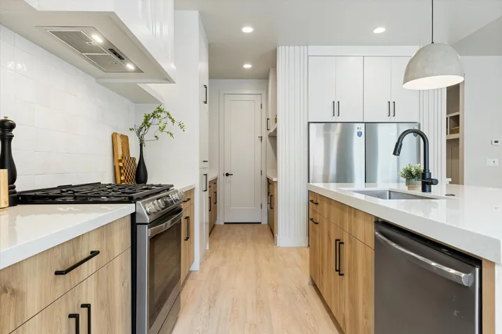 Modern kitchen featuring a gas range, stainless steel appliances, a large island with an undermount sink, light wood-finish cabinetry, and white countertops