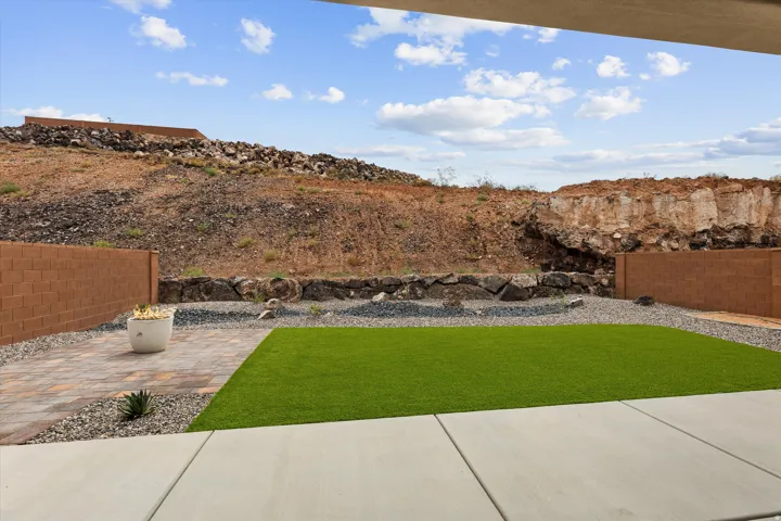 Expansive outdoor living area featuring a rectangular artificial turf lawn, a paver patio, concrete slab flooring, and a low maintenance gravel perimeter