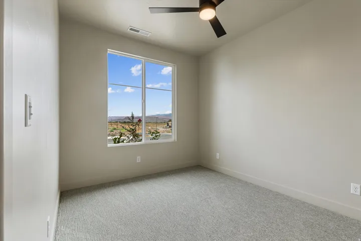 Neutral-toned room featuring a large window, light gray carpet, and a modern ceiling fan