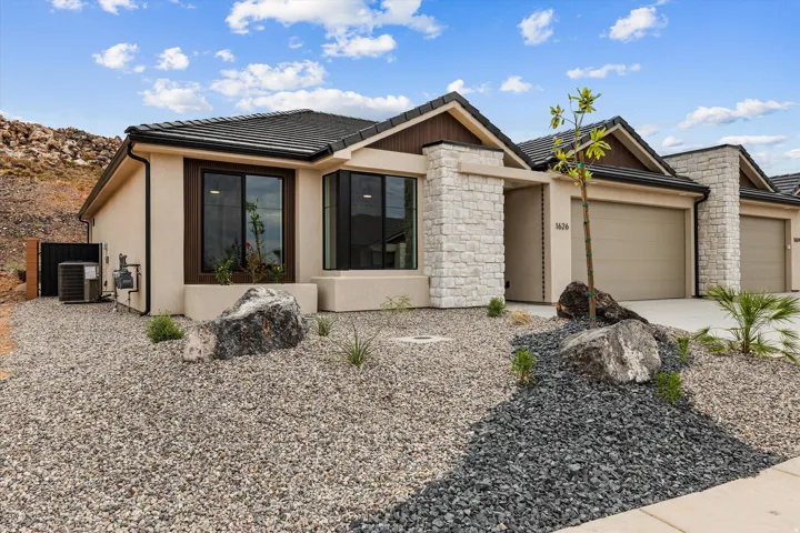 Contemporary stucco exterior with stone accents, dark-framed windows, and a multi-tone gravel landscape