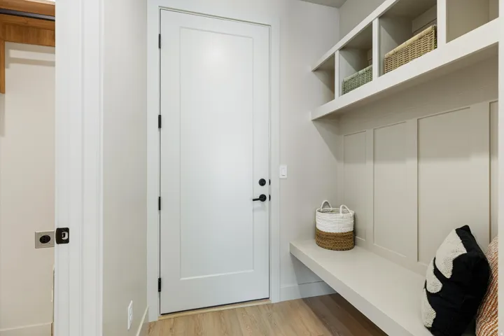 Entryway mudroom featuring a built-in bench, upper shelving, paneled walls, and wood-finish flooring