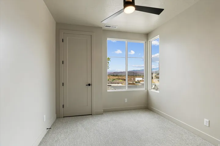 Light-filled interior space featuring broad windows offering landscape views, neutral-toned carpeting, a modern ceiling fan with integrated lighting, and a contemporary flat-panel interior door with matte black hardware