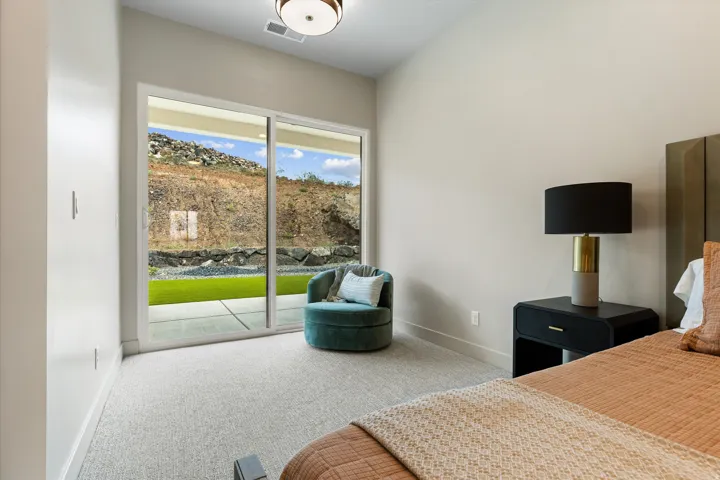 Sliding glass door opening to an outdoor patio with artificial turf and a rock retaining wall