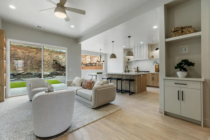 Open-concept living space featuring wood-finish flooring, a contemporary kitchen with a central island, and abundant natural light from a sliding glass door