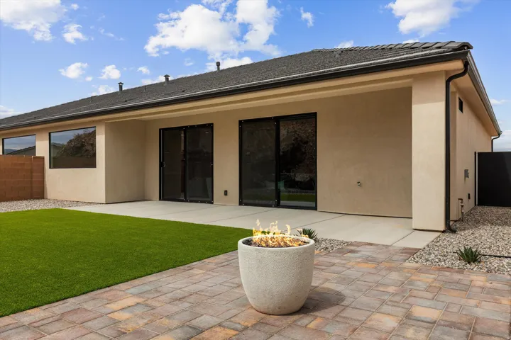 Rear exterior featuring a covered concrete patio, paver patio, artificial turf, and a built-in fire pit