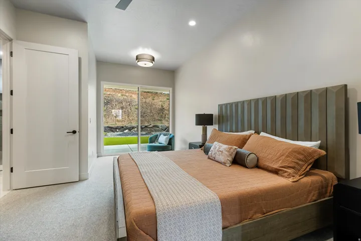 Expansive bedroom featuring a vaulted ceiling with recessed lighting, large sliding glass doors, light-toned carpet flooring, and a contemporary panel headboard