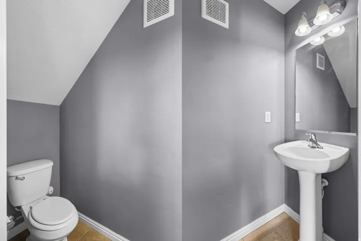 Powder room featuring a pedestal sink with chrome faucet, wall-mounted mirror, and a three-light vanity fixture