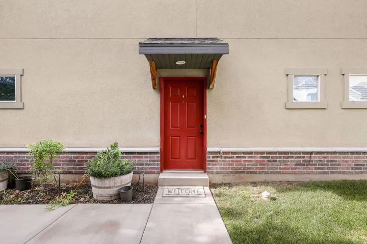Red paneled entry door with an overhead awning, stucco exterior, and a brick accent foundation