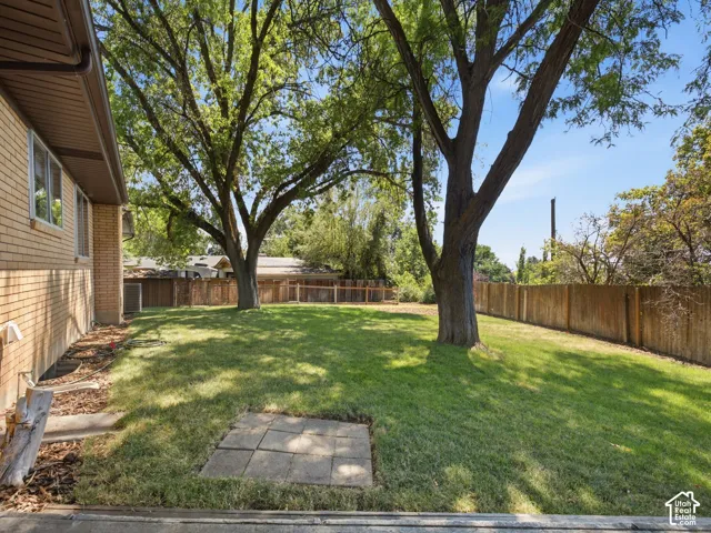 Spacious backyard featuring a manicured lawn, established shade trees, and privacy fencing