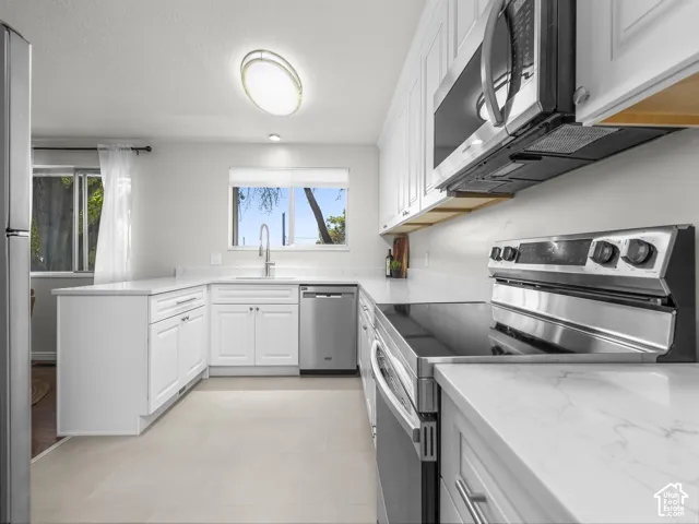 Bright kitchen featuring white shaker cabinetry, stainless steel appliances, light-toned countertops, and wood-finish flooring