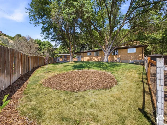 Expansive backyard featuring a manicured lawn and mature trees, offering a full privacy fence along the perimeter, and a circular mulched area
