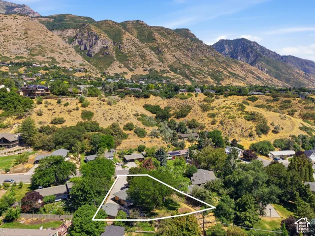 Aerial perspective showcasing a property outlined in white, set amidst a mountainous landscape with established trees and surrounding residences