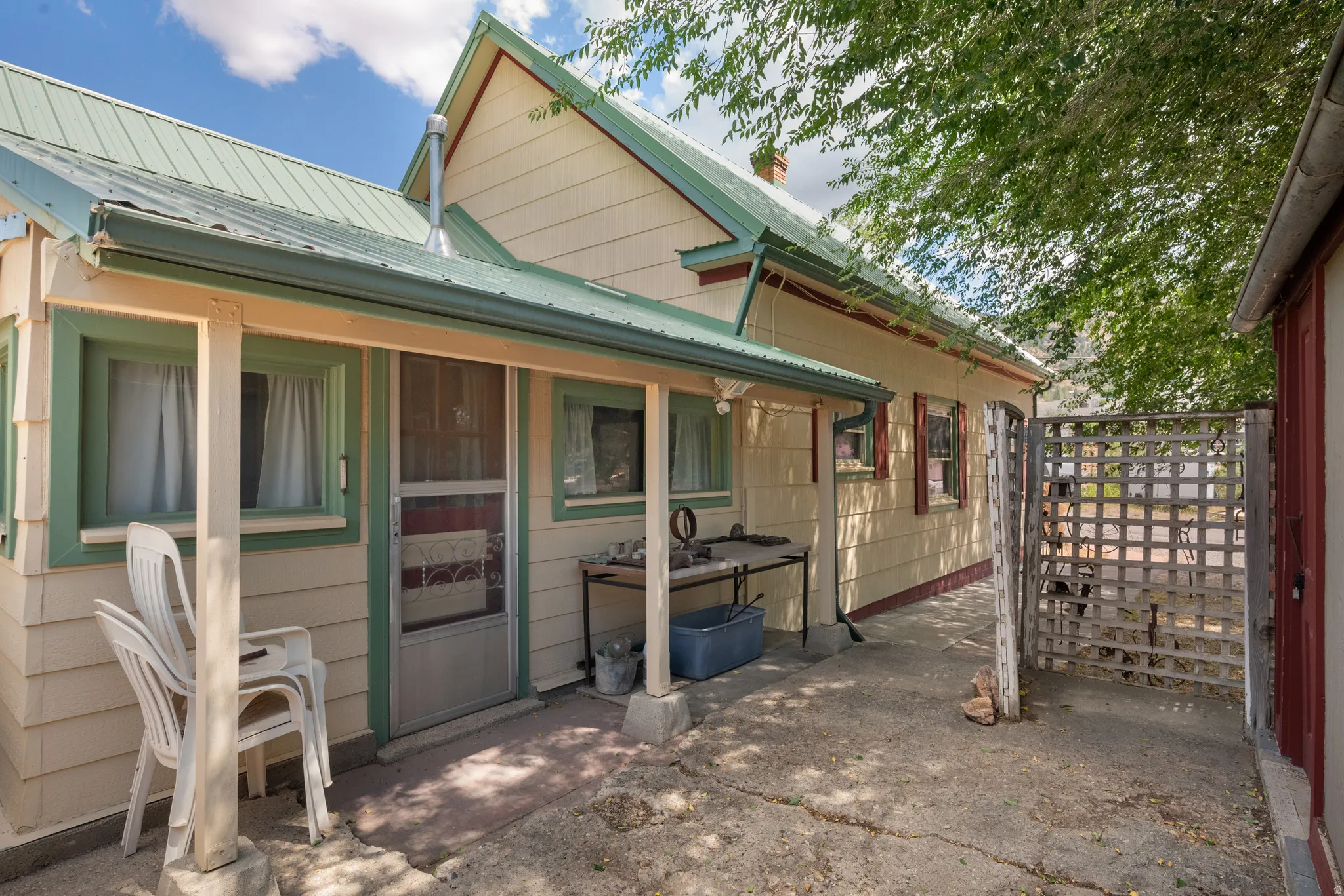 Exterior featuring a green metal roof, light-colored siding, covered porch, and a lattice fence