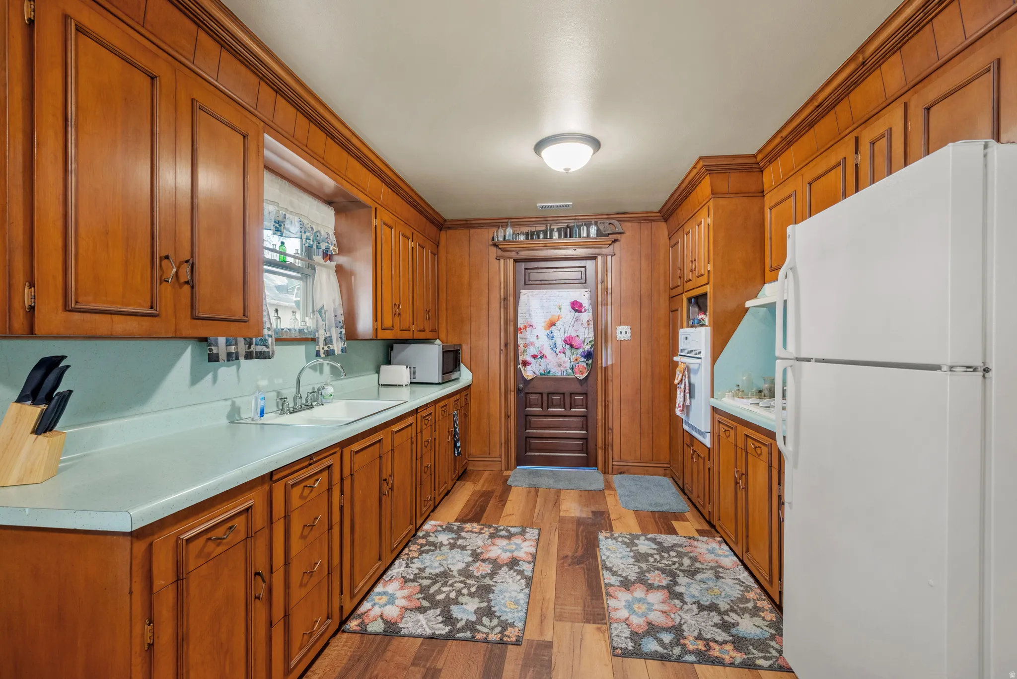 Kitchen featuring extensive wood cabinetry, wood-finish flooring, a double basin sink, and ample countertop space