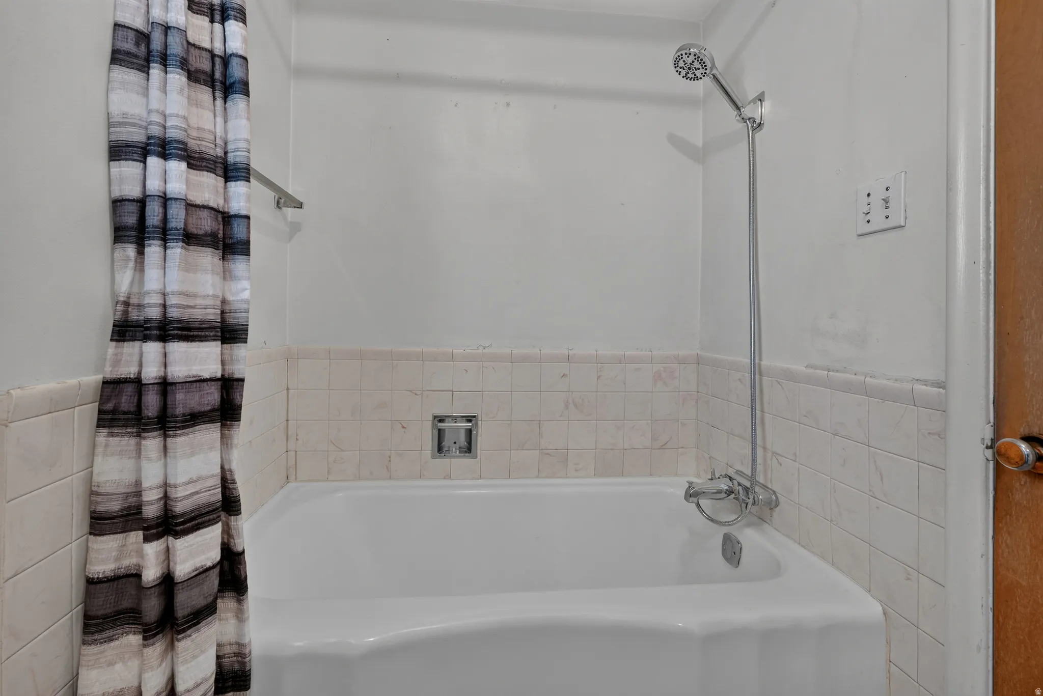White porcelain bathtub with integrated shower, chrome fixtures, and tiled surround