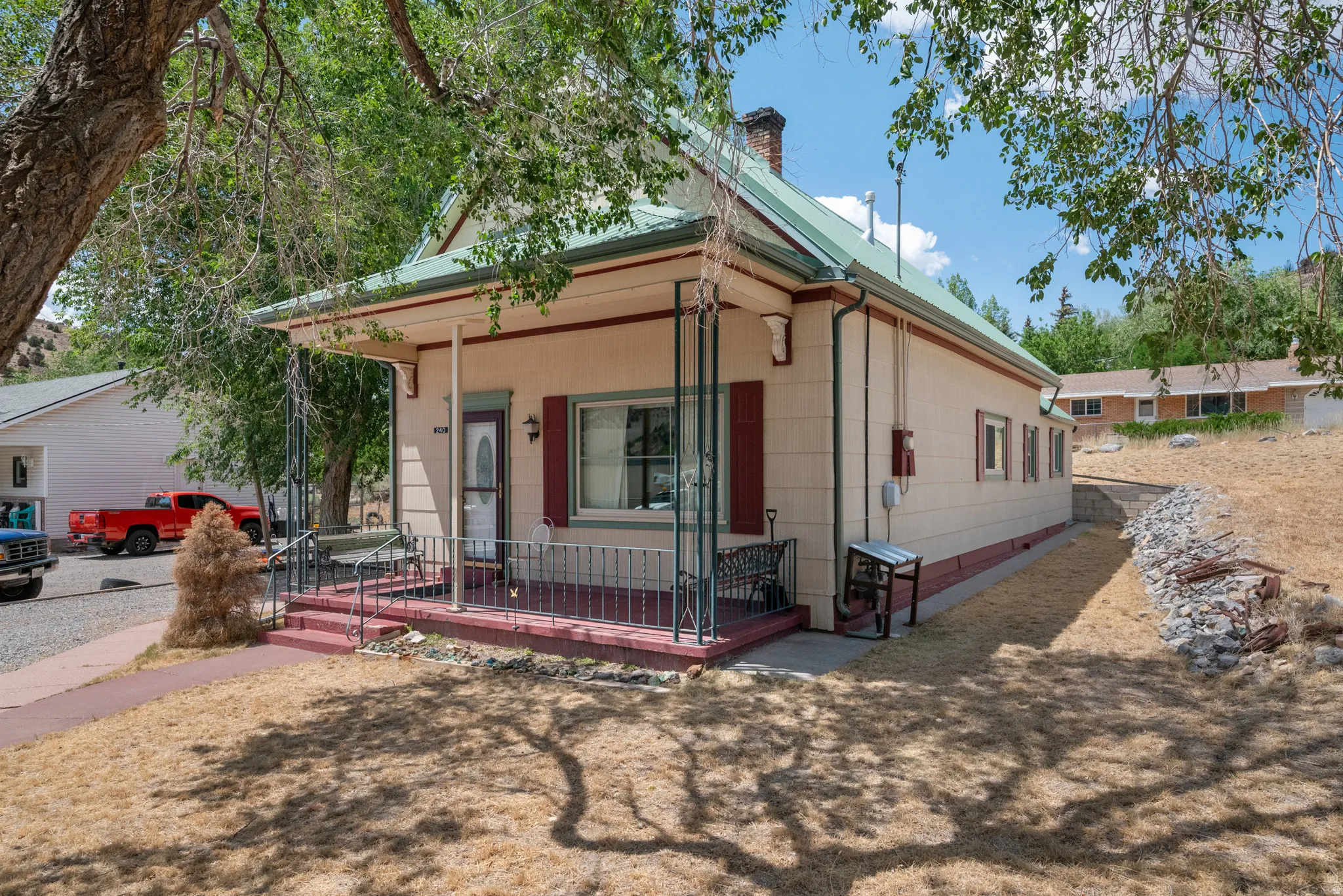 Front exterior featuring a covered porch with decorative metal railing, a green metal roof, and red window shutters