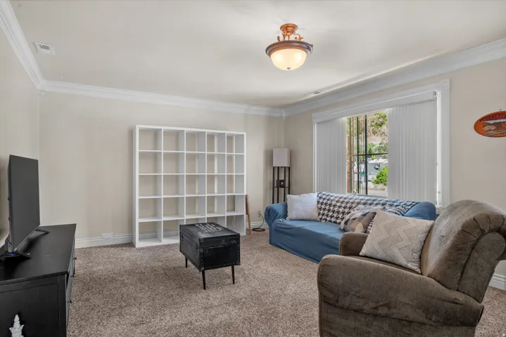 Inviting living space featuring textured carpet flooring, neutral wall tones, and crown molding