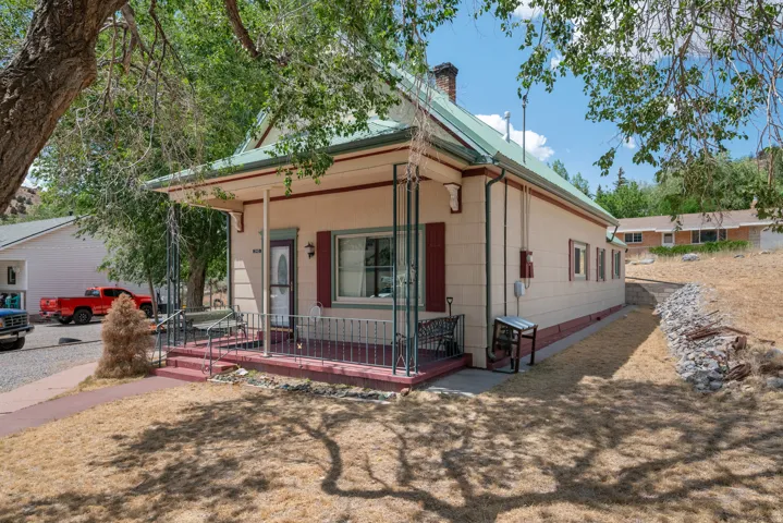 Front exterior featuring a covered porch with decorative metal railing, a green metal roof, and red window shutters