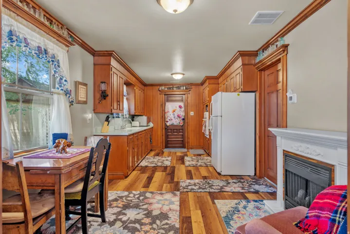 Kitchen and dining area featuring warm wood cabinetry, light countertops, wood-finish flooring, and a fireplace with a white mantel