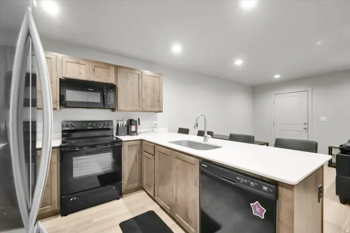 Kitchen featuring light wood-finish cabinetry, light countertops, and black appliances including an oven/range, microwave, and dishwasher