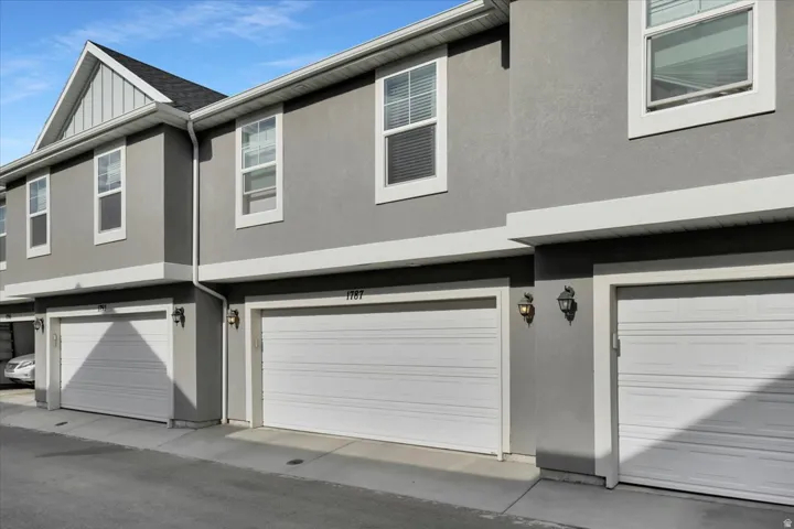 Multi-story stucco exterior featuring white-framed windows, white garage doors, and individual exterior lighting fixtures