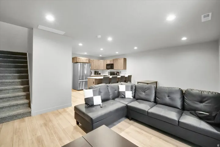 Open-concept living area with wood-finish flooring, recessed lighting, and a carpeted staircase
