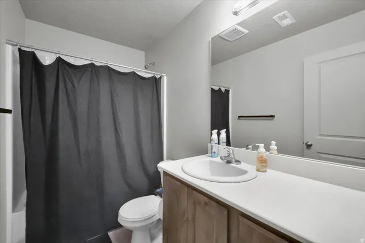 Bathroom featuring a bathtub with shower fixture, toilet, vanity with integrated sink, and a large wall-mounted mirror