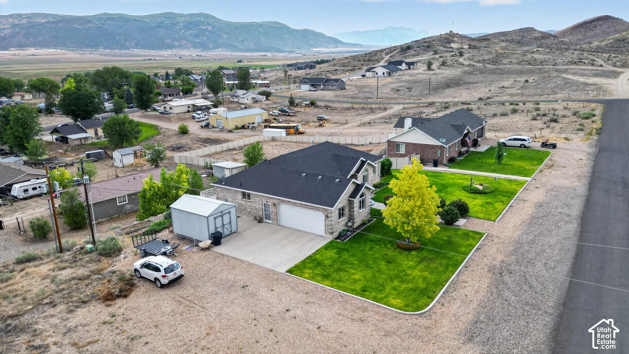 Stone veneer exterior with an attached two-car garage, dark asphalt shingle roof, landscaped front yard with mature trees and green lawn, and a paved driveway