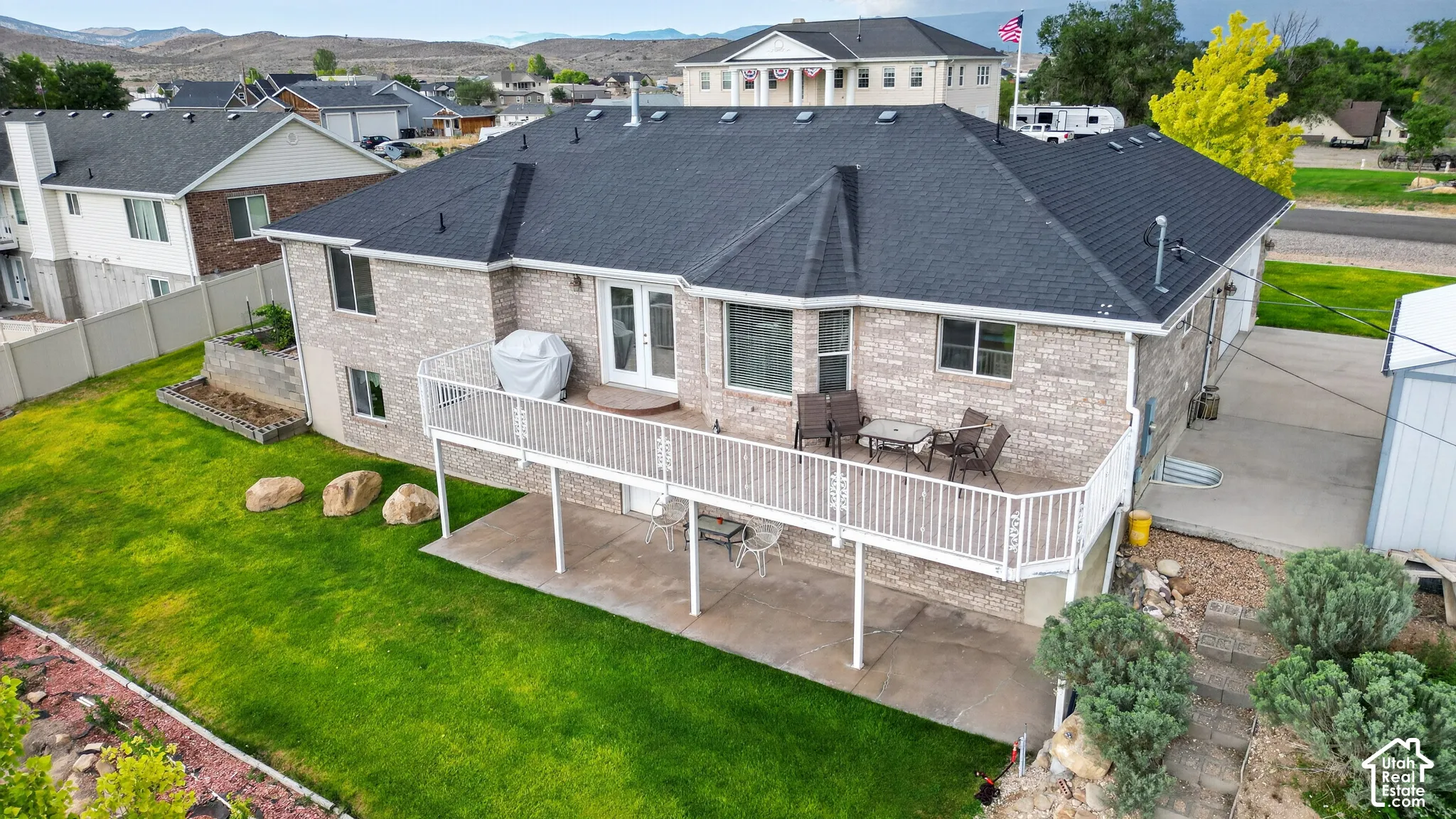 Rear exterior featuring a full-width deck with white railing, a lower-level concrete patio, and a manicured lawn