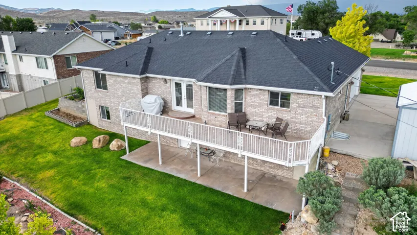 Rear exterior featuring a full-width deck with white railing, a lower-level concrete patio, and a manicured lawn