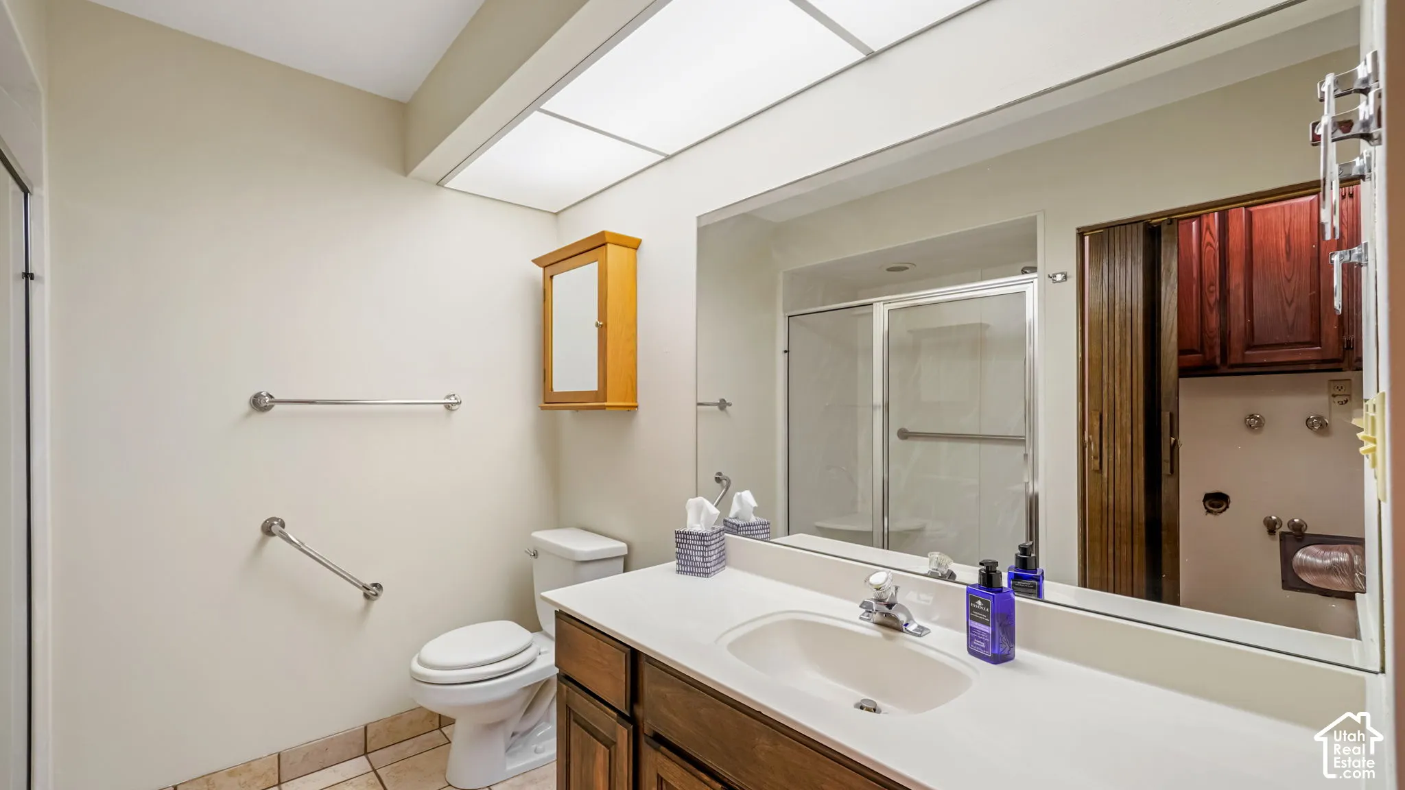 Bathroom featuring a white vanity with integrated sink, wood-finish cabinetry, a large wall-mounted mirror, and a fluorescent ceiling light
