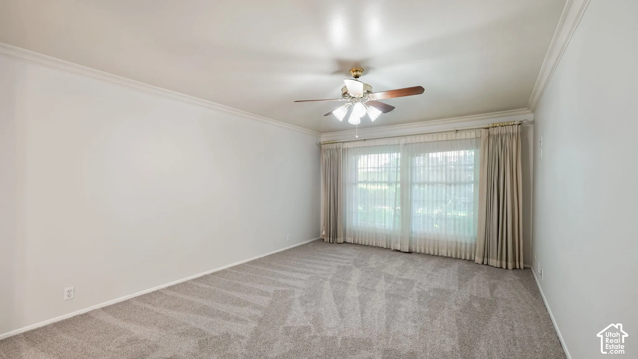 Spacious room featuring light gray patterned carpeting, white walls, crown molding, and a ceiling fan with light fixture