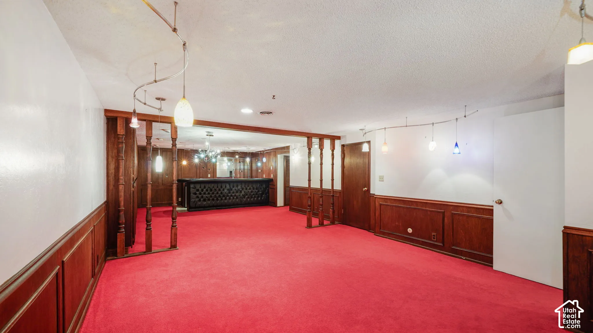 Spacious room featuring red carpeting, wood paneling, multiple doors, and a built-in bar with tufted detailing